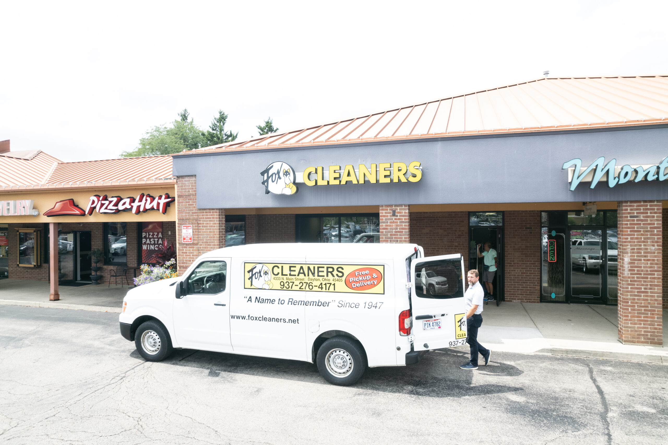 A white delivery van for Fox Cleaners is parked outside a storefront in a strip mall, with a person standing at the van’s open door—providing convenient dry cleaning near me for customers in the area. A white delivery van for Fox Cleaners is parked outside a storefront in a strip mall, with a person standing at the van’s open door—providing convenient dry cleaning near me for customers in the area.