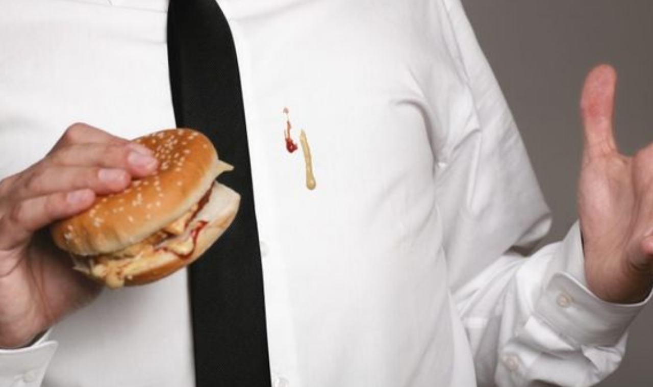 Person holding a sandwich dropped ketchup and mustard onto the front of their white dress shirt and black tie.